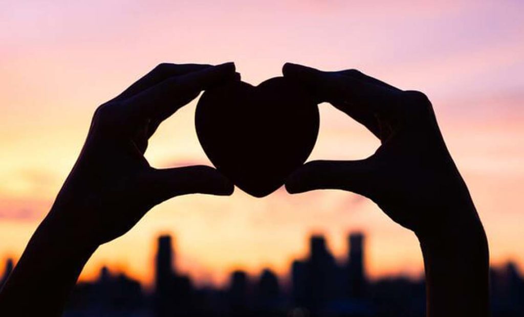 Two hands holding up a heart at sunset