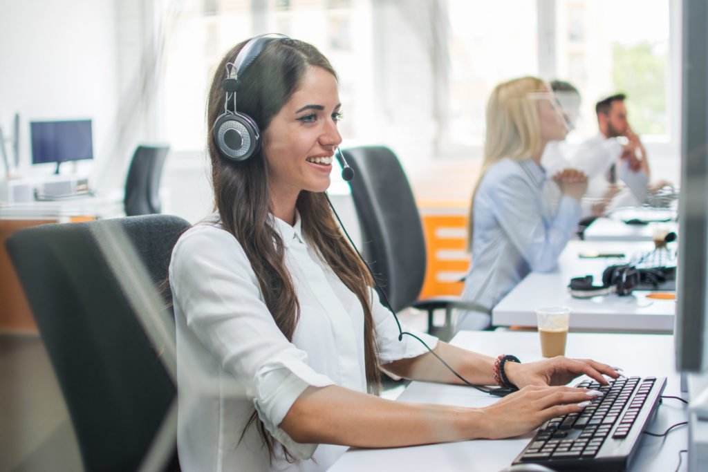 Smiling business woman with hands-free set working on computer and giving instructions online to customer.